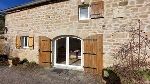 A stone building with a large arched doorway, wooden shutters, and a small window. - la Longere du Haut Courby en Plein Cœur de la Forêt Domaniale de Sédières (Eyrein)