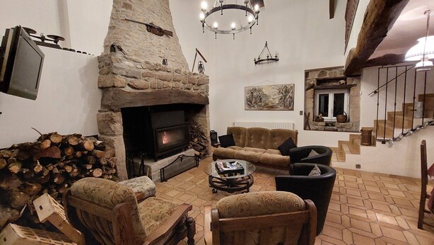 A cozy living room with a stone fireplace, a television, and a staircase leading to an upper level. - la Longere du Haut Courby en Plein Cœur de la Forêt Domaniale de Sédières (Eyrein)