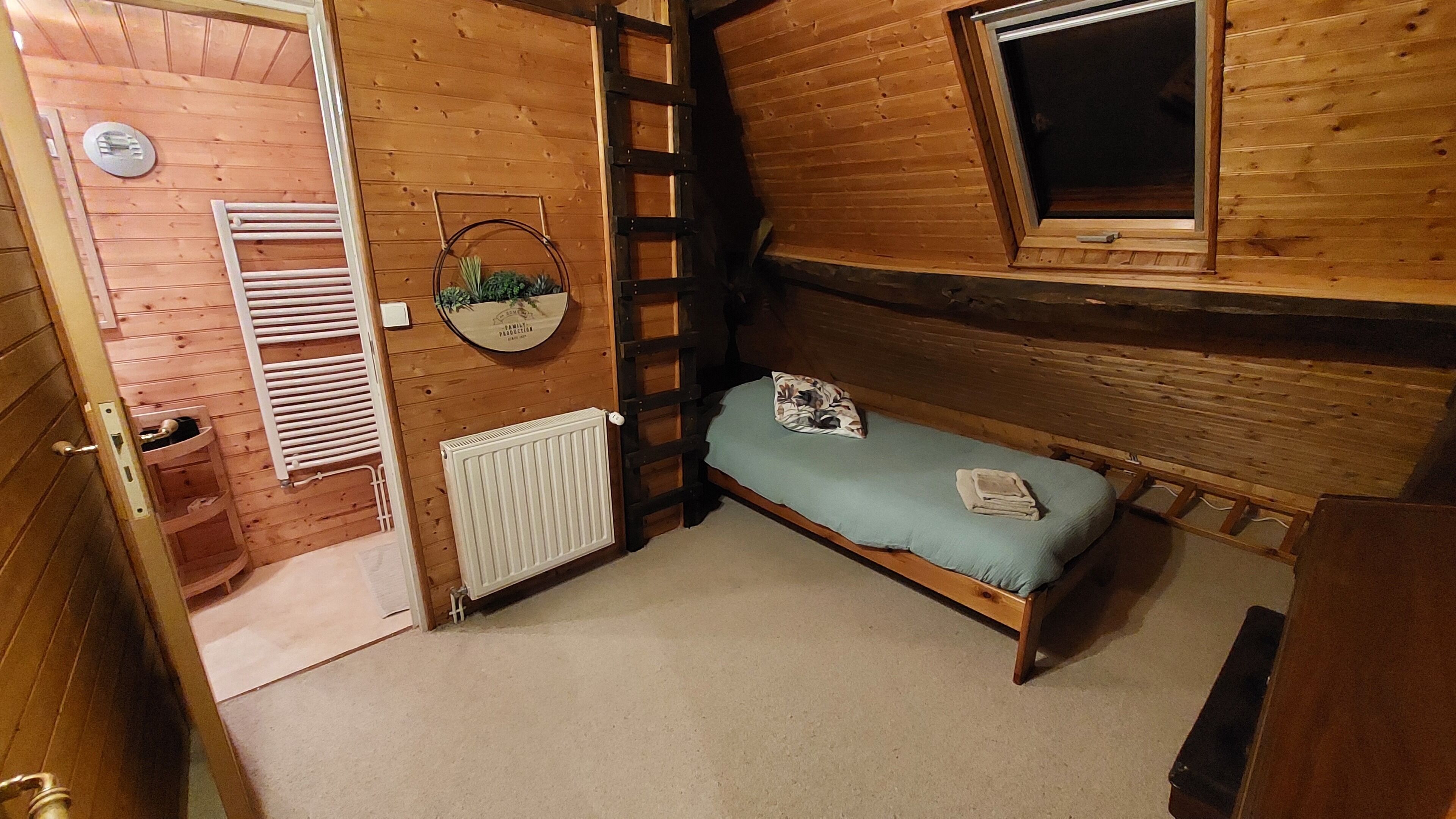 Une petite pièce agréable, dotée d’un lit simple, d’un radiateur, d’une fenêtre et d’une porte en bois.