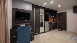 Une chambre d’hôtel moderne équipée d’un téléviseur à écran plat, d’un bureau avec un téléphone, d’une chaise bleue, d’un placard à portes coulissantes et d’un petit coin cuisine.