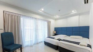 Une chambre d’hôtel avec deux lits, une chaise et une grande fenêtre avec des rideaux légers.