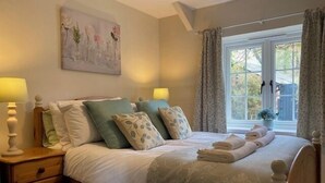 Uma cama bem arrumada com colcha estampada, duas mesas de cabeceira com abajures e uma janela com cortinas.