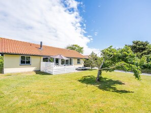 Een gelijkvloers huis met een pannendak, een overdekt terras en een klein gazon.