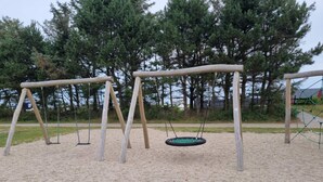 A playground with two swings and a tire swing on a sandy surface, surrounded by trees and a fence. - 5 Star Holiday Home in Tarm (Tarm)
