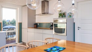A modern kitchen with a wooden dining table, two pendant lights, and a built-in oven. - 5 Star Holiday Home in Tarm (Tarm)