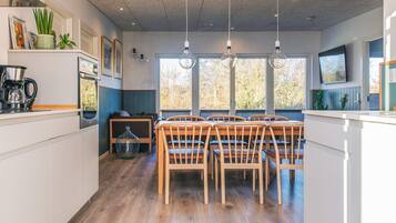 Una cocina moderna con sillas de madera, una máquina de café y un ventanal grande.