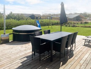 En træterrasse med et boblebad, et bord med stole og et gyngestativ i baggrunden.