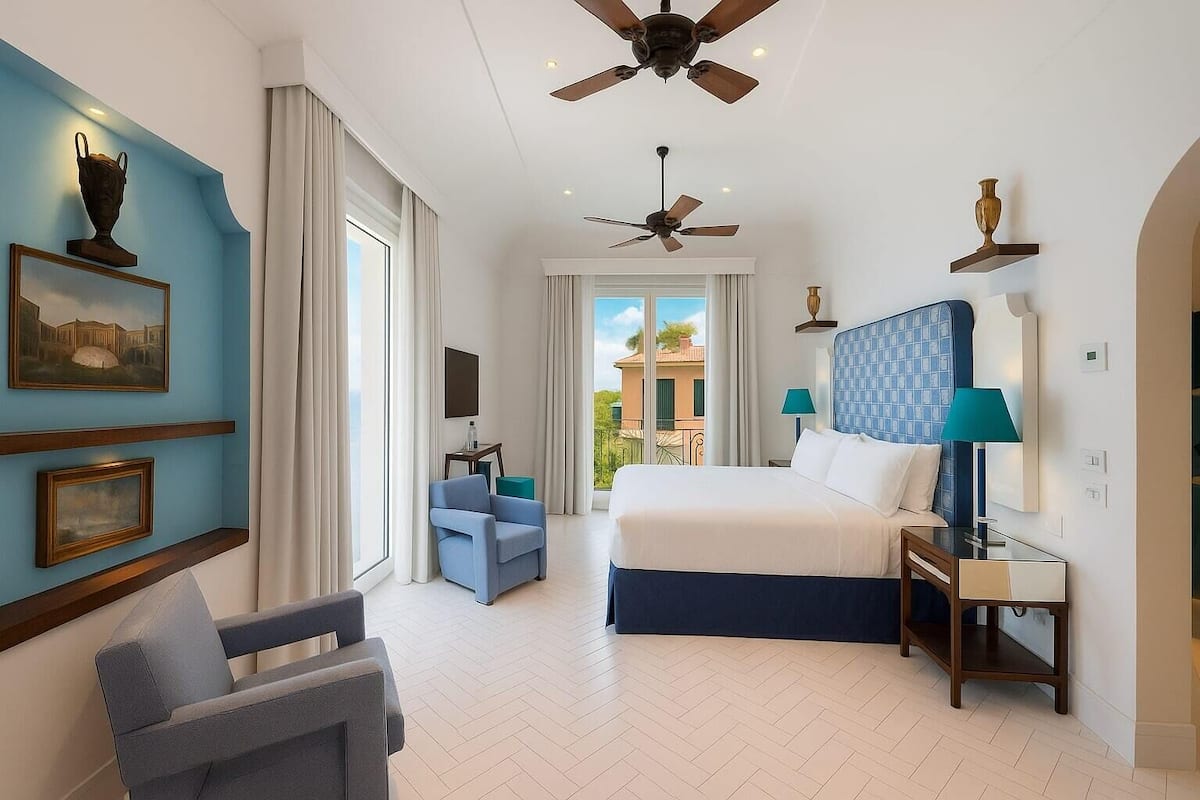 A hotel room with a bed, a chair, a desk, a ceiling fan, and a balcony view.