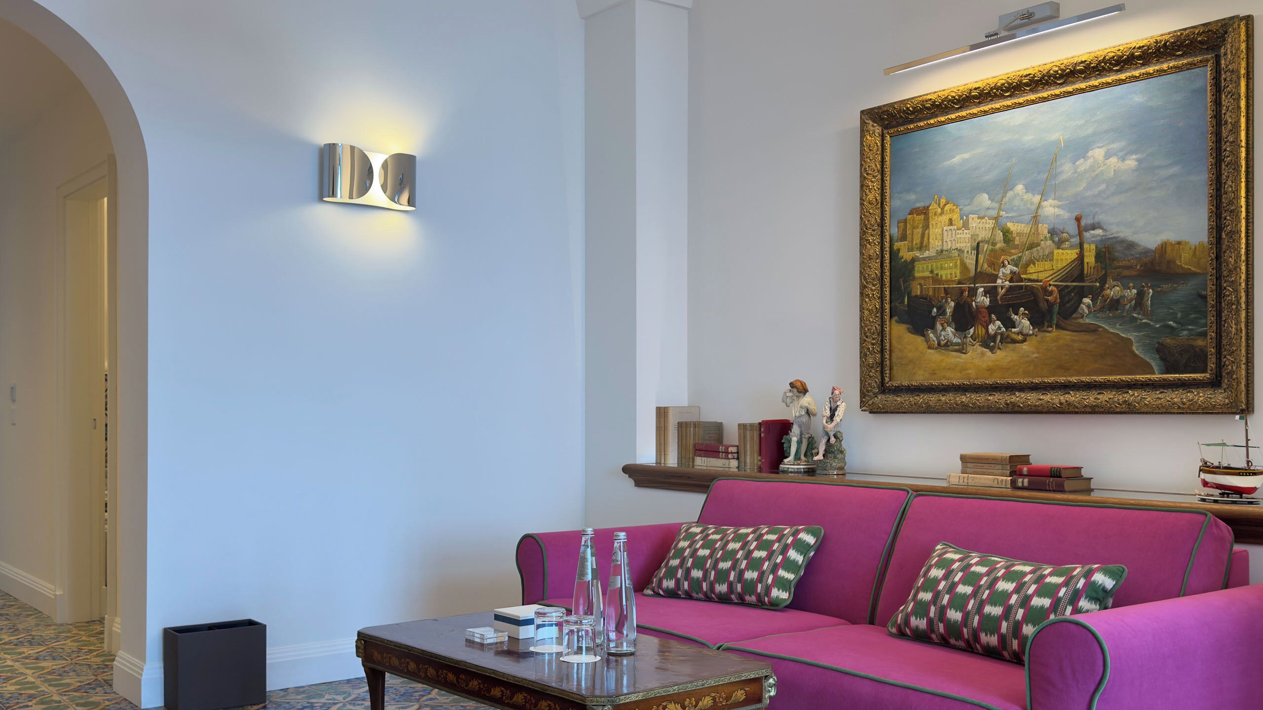 A living room with a pink sofa, a painting, and a small table with decorative items.