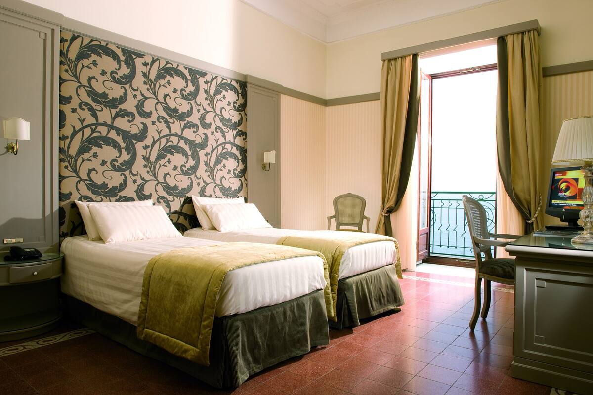 Une chambre d’hôtel avec deux lits, un bureau, une chaise et une fenêtre avec des rideaux.