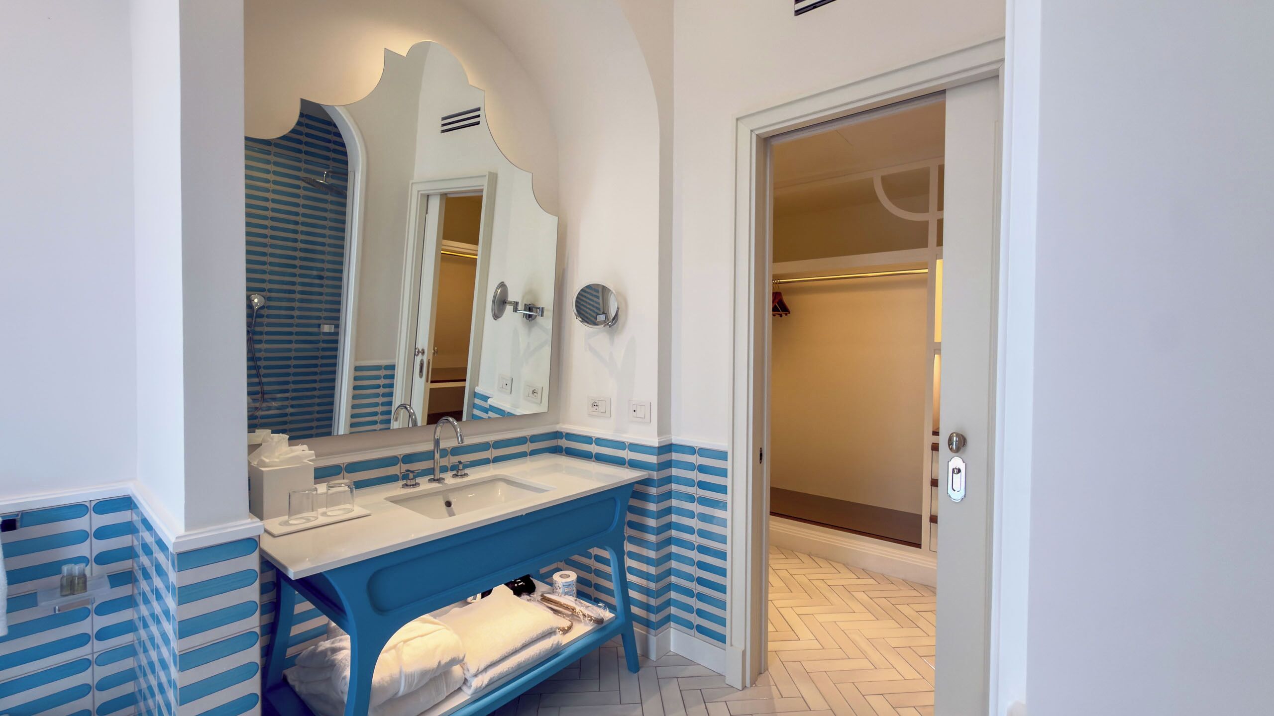 A bathroom with a white sink, blue-striped tiles, a mirror, and a shower area.