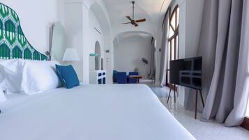 Habitación de hotel con una cama grande, ventilador de techo, televisor sobre un mueble y vista al pasillo.