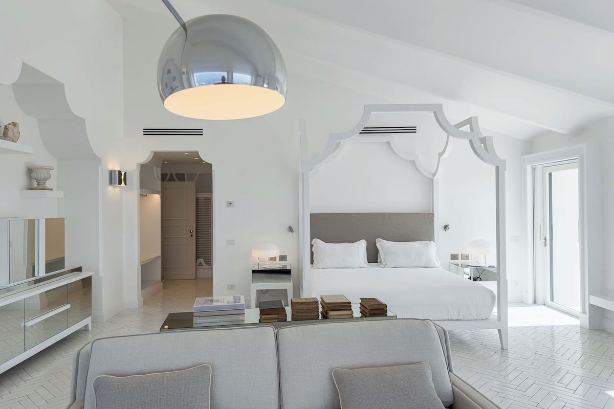 A modern bedroom with a canopy bed, a sofa, a glass coffee table, and a pendant light.
