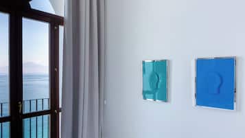 Una habitación con un ventanal grande con vista al mar, una cortina y dos cuadros en la pared.