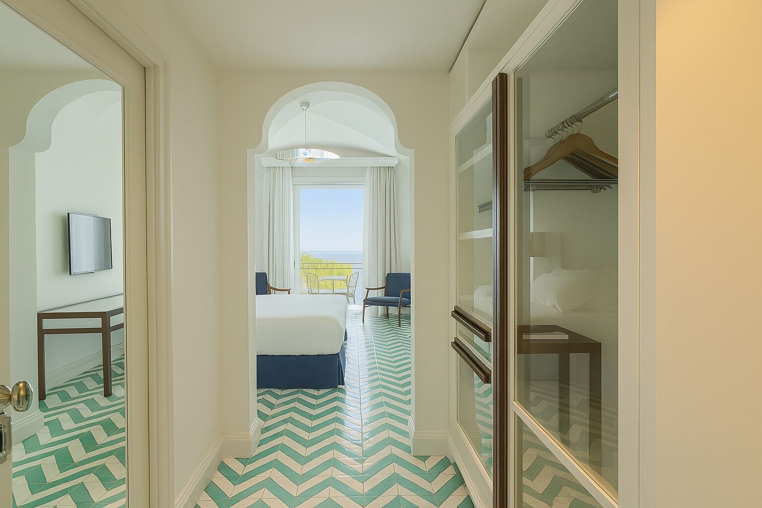 A hotel room with a bed, a seating area with chairs, a television, and a view of the outdoors.