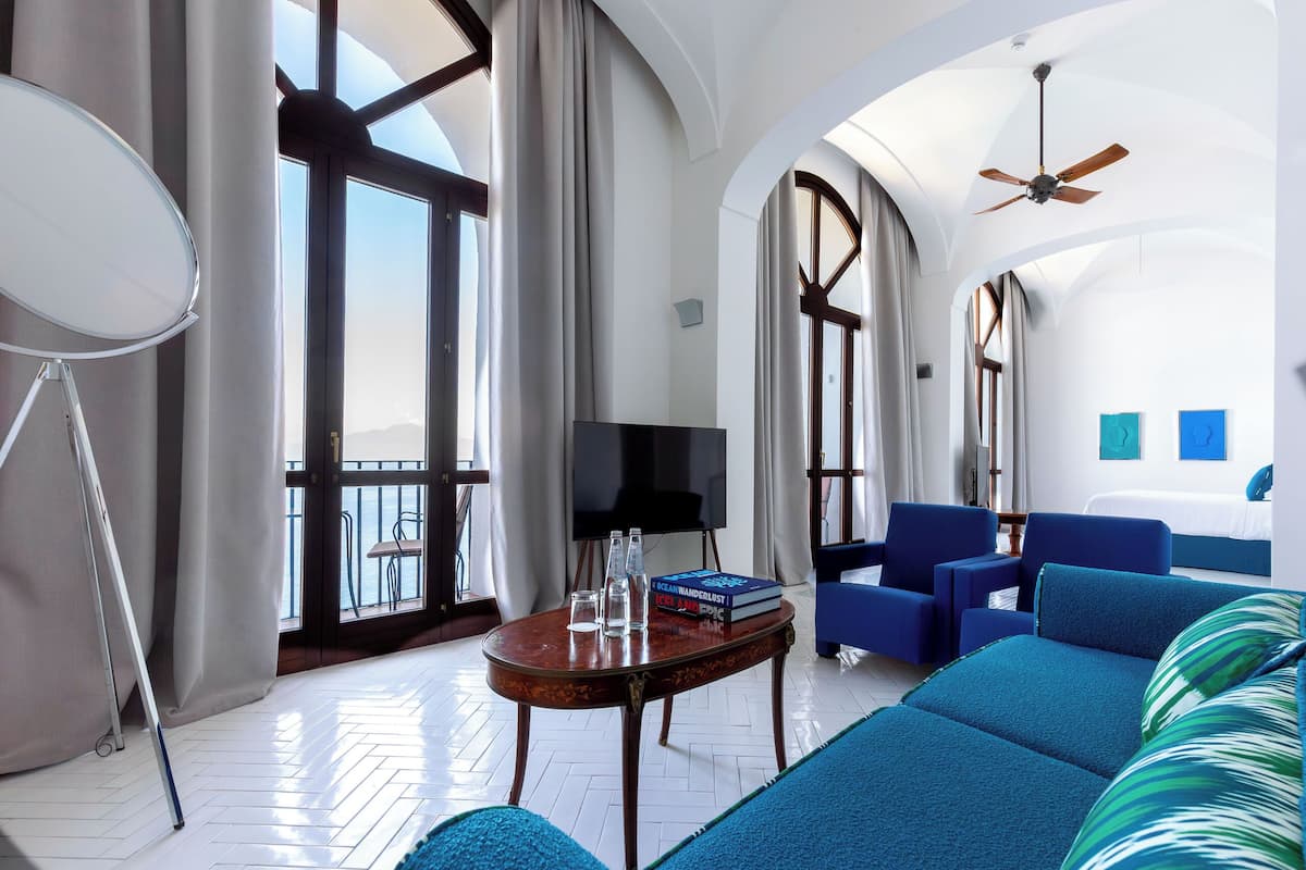 A spacious living room with a large window, a flat-screen TV, a wooden coffee table, and a blue sofa.