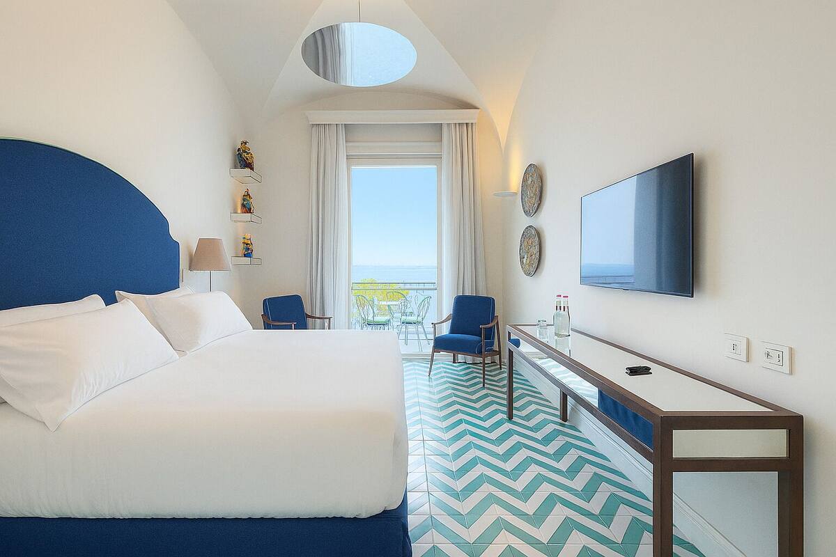 A hotel room with a large bed, a desk, a chair, a television, and a view of the outdoors.