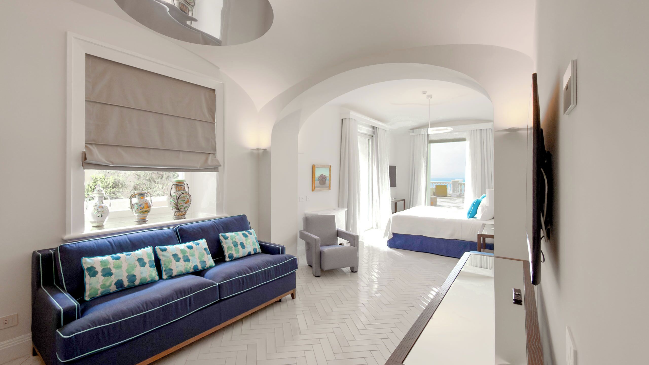 A hotel room with a sofa, armchair, bed, and a view of the sea.