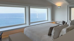 A bedroom with a large bed, a desk, and a view of the ocean.