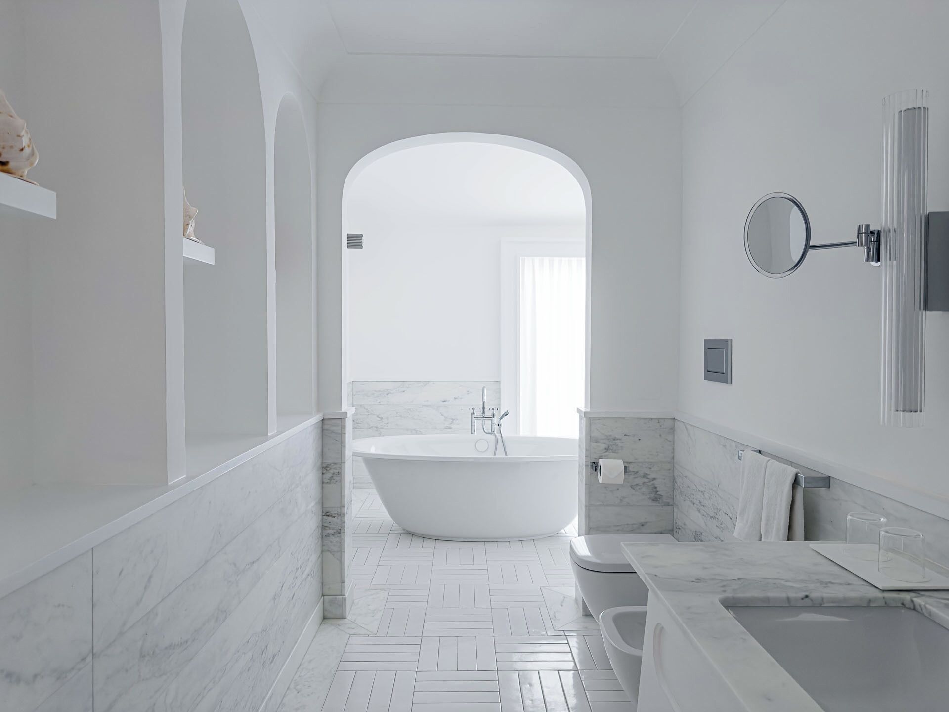Un baño moderno con una bañera independiente, un tocador con espejo y un suelo con estampado en espiga.