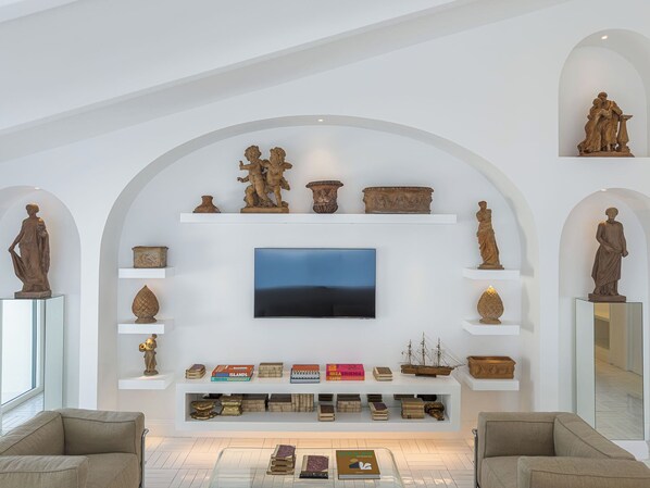 A modern living room with a flat-screen TV, classical sculptures, and a collection of books and decorative items on shelves. - Grand Hotel Europa Palace (Sorrento)