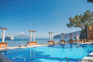 A pool with lounge chairs and umbrellas, a cruise ship in the background, and a mountain view. - Grand Hotel Europa Palace (Sorrento)