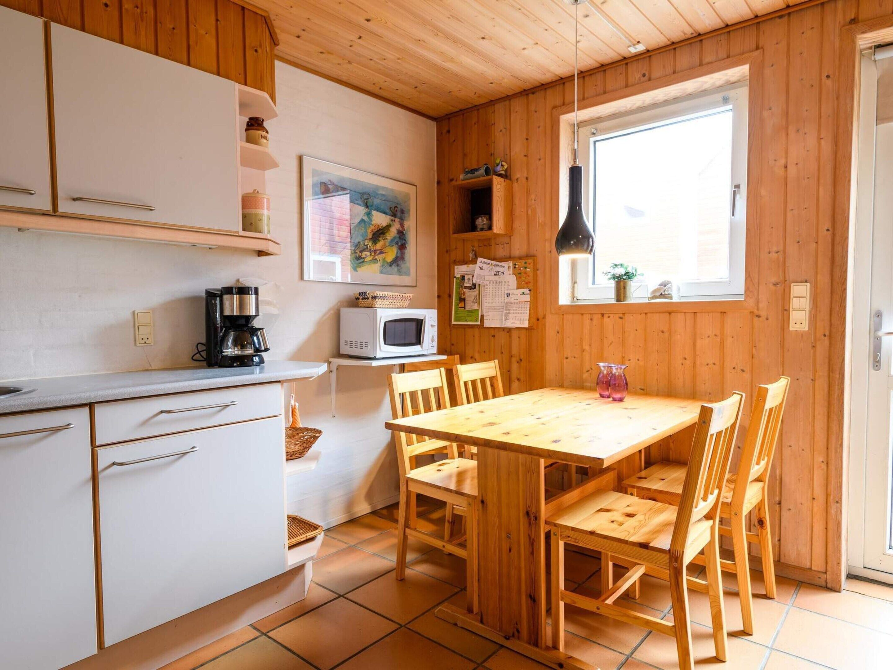 Una cocina con armarios de madera, microondas, cafetera y una mesa de comedor con sillas.