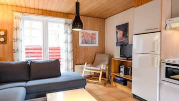A cozy living room with a sofa, a dining table with a candle, a TV, and a white refrigerator.