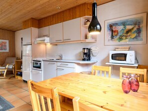 A compact kitchen with white cabinets, a wooden dining table, and a microwave. - 4 Person Holiday Home in Fano (Fano)