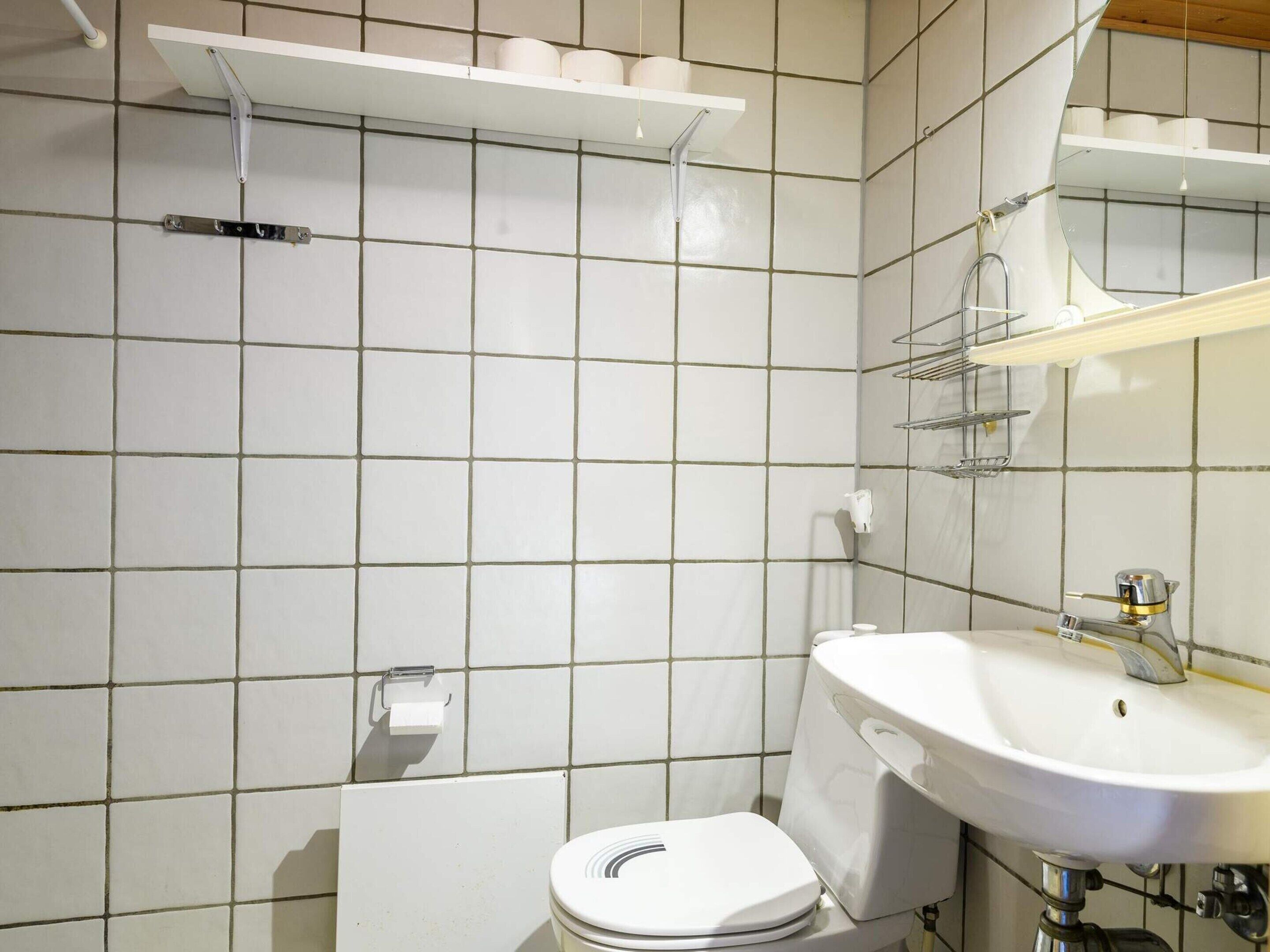 A bathroom with a toilet, sink, and mirror. There are shelves above the toilet and a towel rack on the wall.