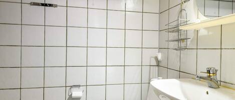 A bathroom with a toilet, sink, and mirror. There are shelves above the toilet and a towel rack on the wall.