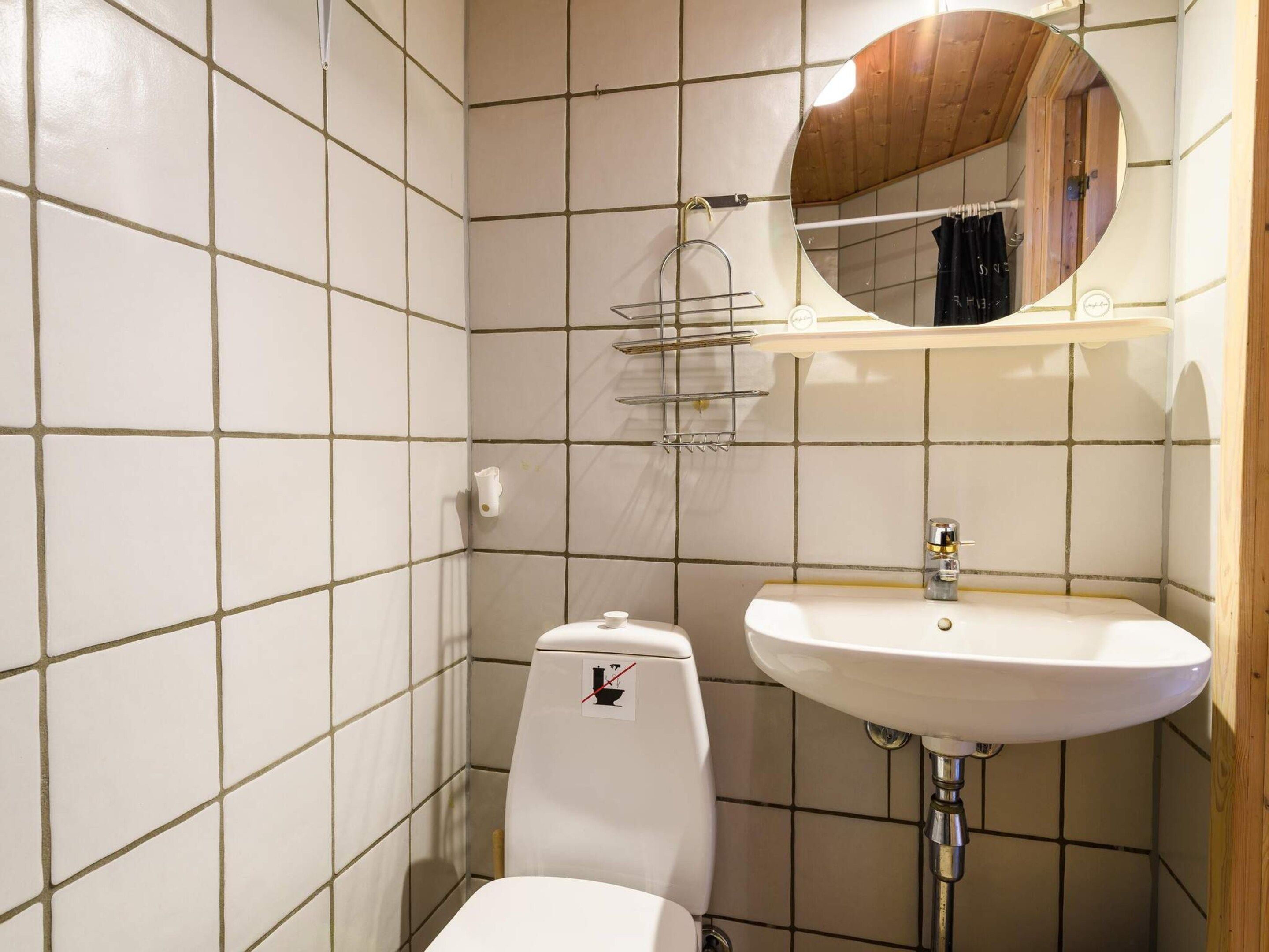 A bathroom with white tiled walls, a white toilet, a sink with a mirror above it, and a towel rack.