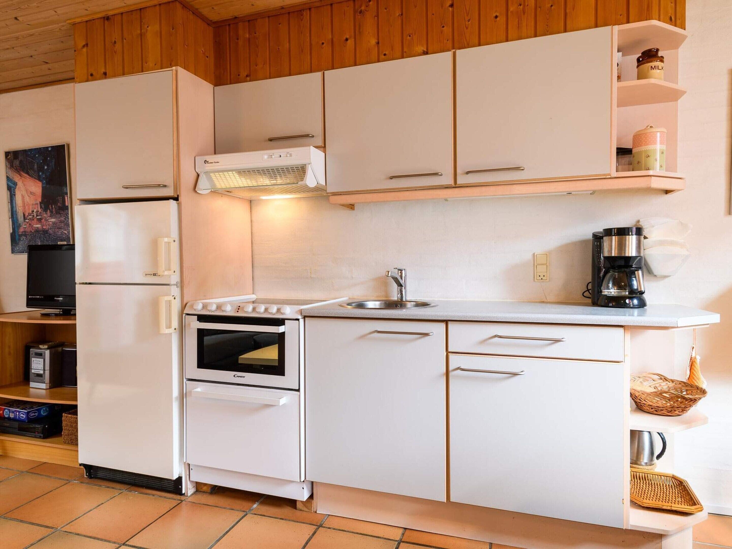 Une cuisine de taille réduite, avec des meubles blancs, une cuisinière, un réfrigérateur et une machine à café.