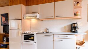 A compact kitchen with white cabinets, a stove, a refrigerator, and a coffee maker. - 4 Person Holiday Home in Fano (Fano)