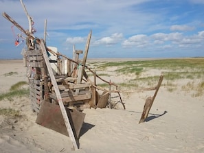 En strandkonstruktion gjord av träplankor och grenar, med en flaska och en flagga.