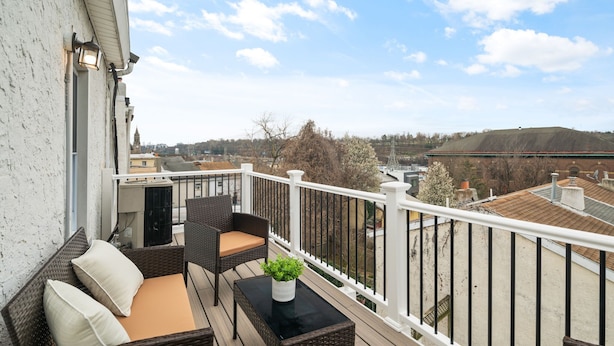 En balkon med fletningsmøbler, et lille bord med en plante, og udsigt til bygninger og træer.