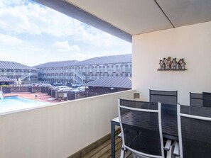 Een balkon met uitzicht op een zwembad en een parkeerplaats, ingericht met zwarte mesh-stoelen en een kleine tafel.