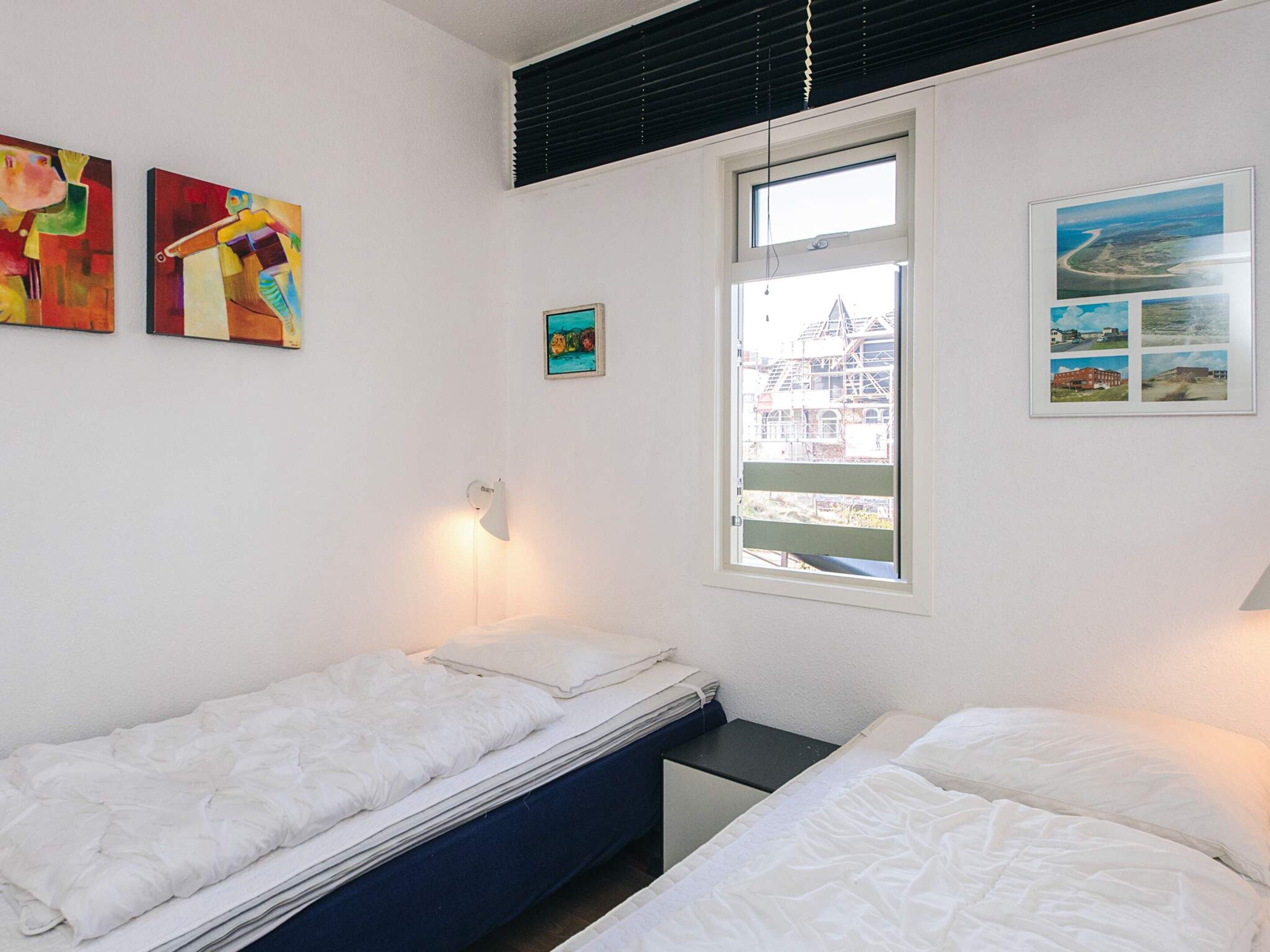 A bedroom with two single beds, a window with a view of buildings, and two pieces of wall art.
