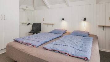 A bedroom with a bunk bed, a chair, a desk, and wall-mounted lamps.