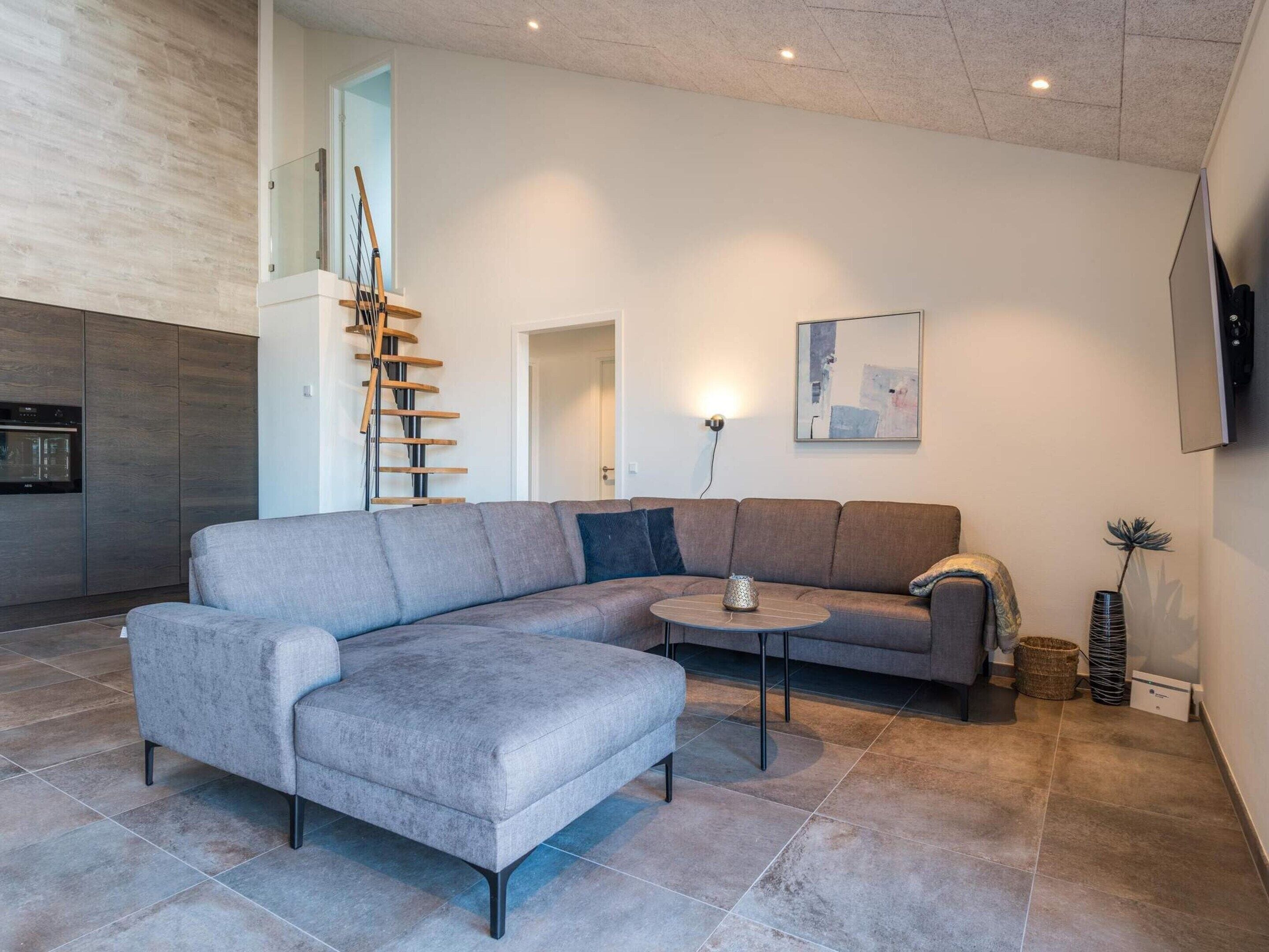 A modern living room with a grey sectional sofa, a small round coffee table, and a staircase with wooden steps.
