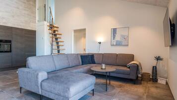 A modern living room with a grey sectional sofa, a small round coffee table, and a staircase with wooden steps.
