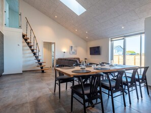 A spacious living area with a dining table, chairs, a sofa, and a staircase.
