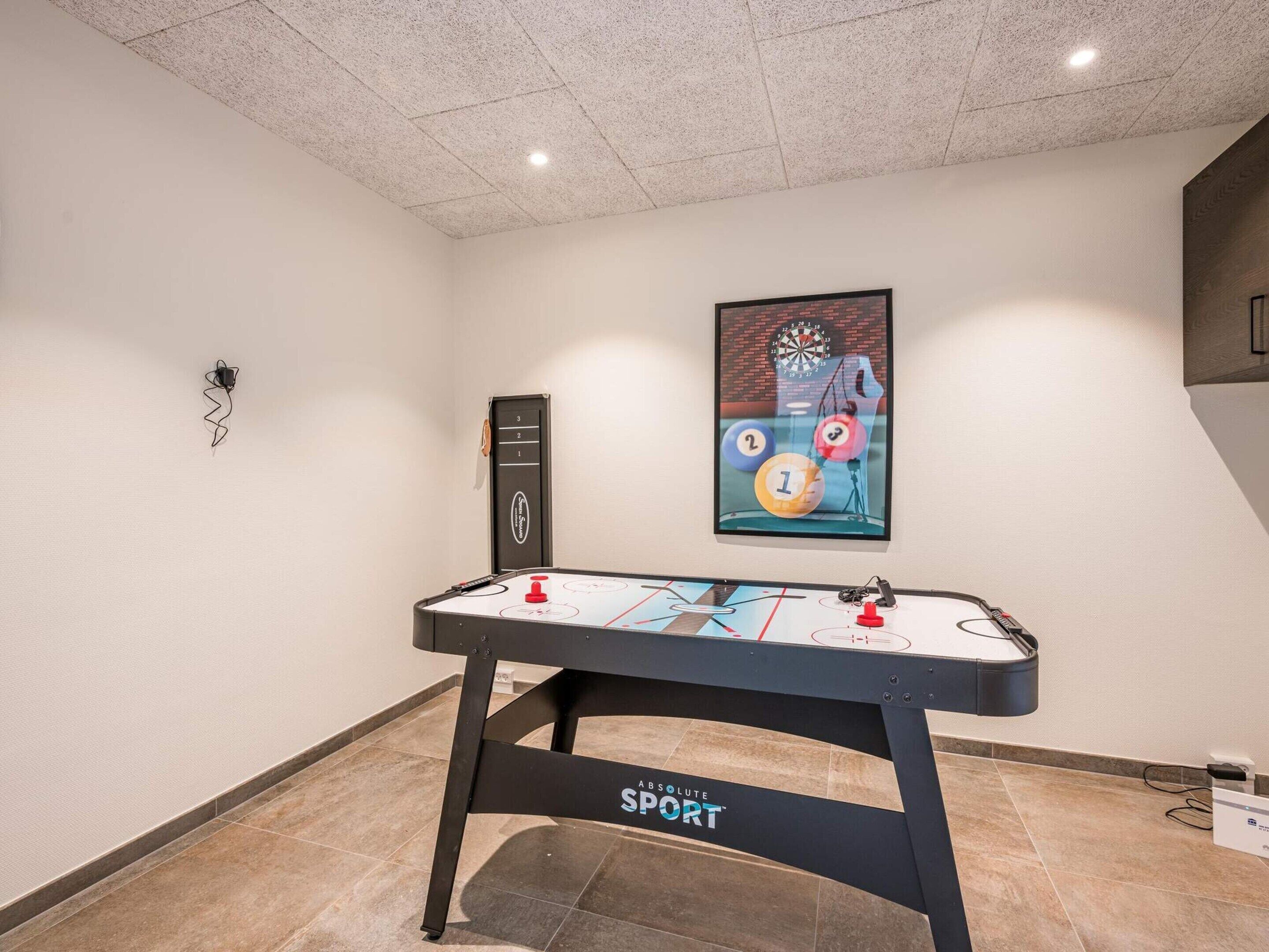 A foosball table with a 'SPORT' logo, a dartboard, and a wall-mounted electrical outlet.