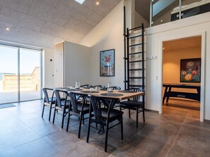 A modern dining area with a high ceiling, a dining table with chairs, and a pool table in the background. - 6 Person Holiday Home in Hvide Sande (Hvide Sande)