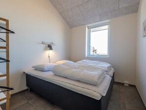 Quarto com cama, mesa de cabeceira, abajur, janela e escada de madeira.