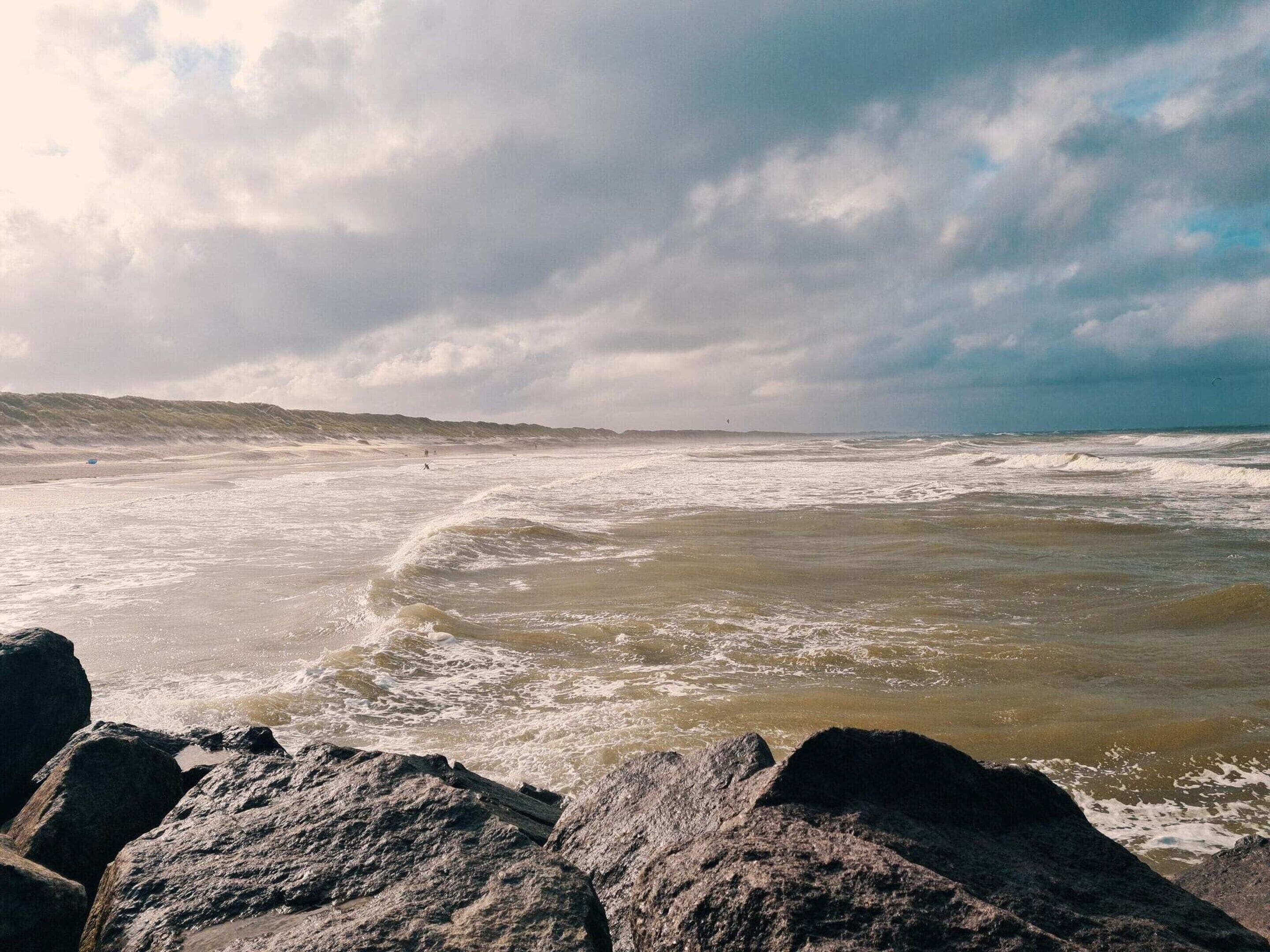 A coastal landscape with large rocks in the foreground and a view of the sea under a cloudy sky.