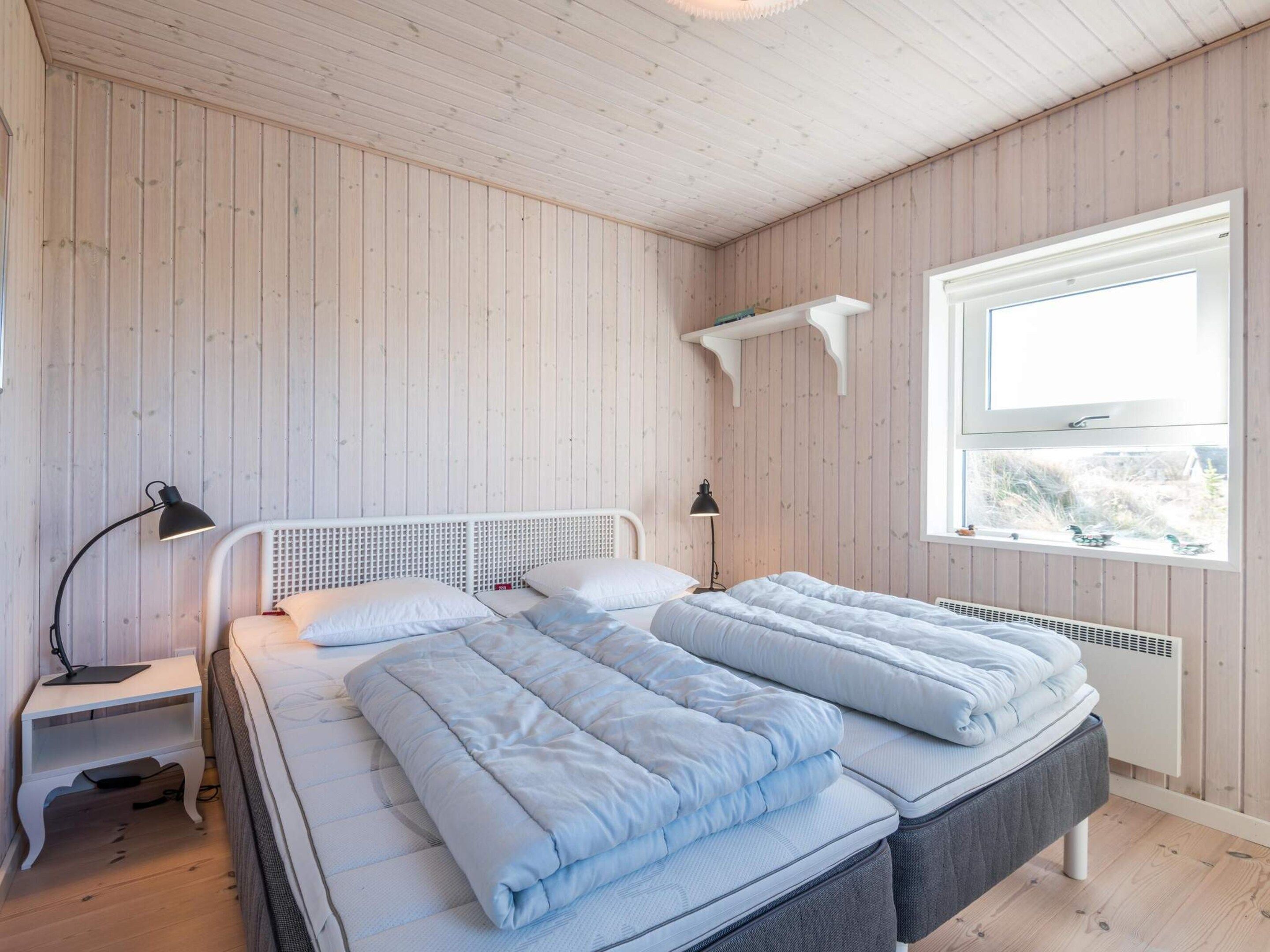 A room with a bed, bedside tables, a window, and wooden walls.