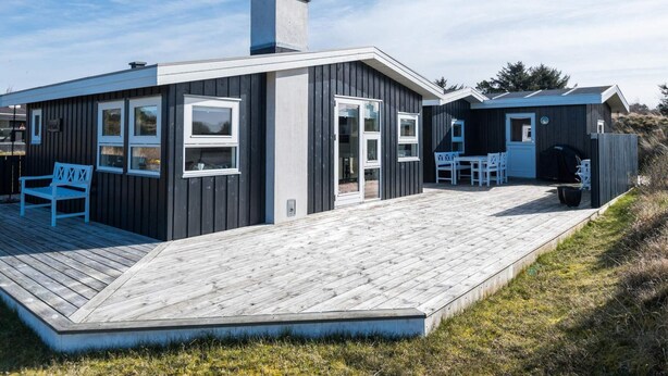 A modern cabin with a deck, a covered outdoor seating area, and a separate building with a chimney. - 4 Person Holiday Home in Fano (Fano)