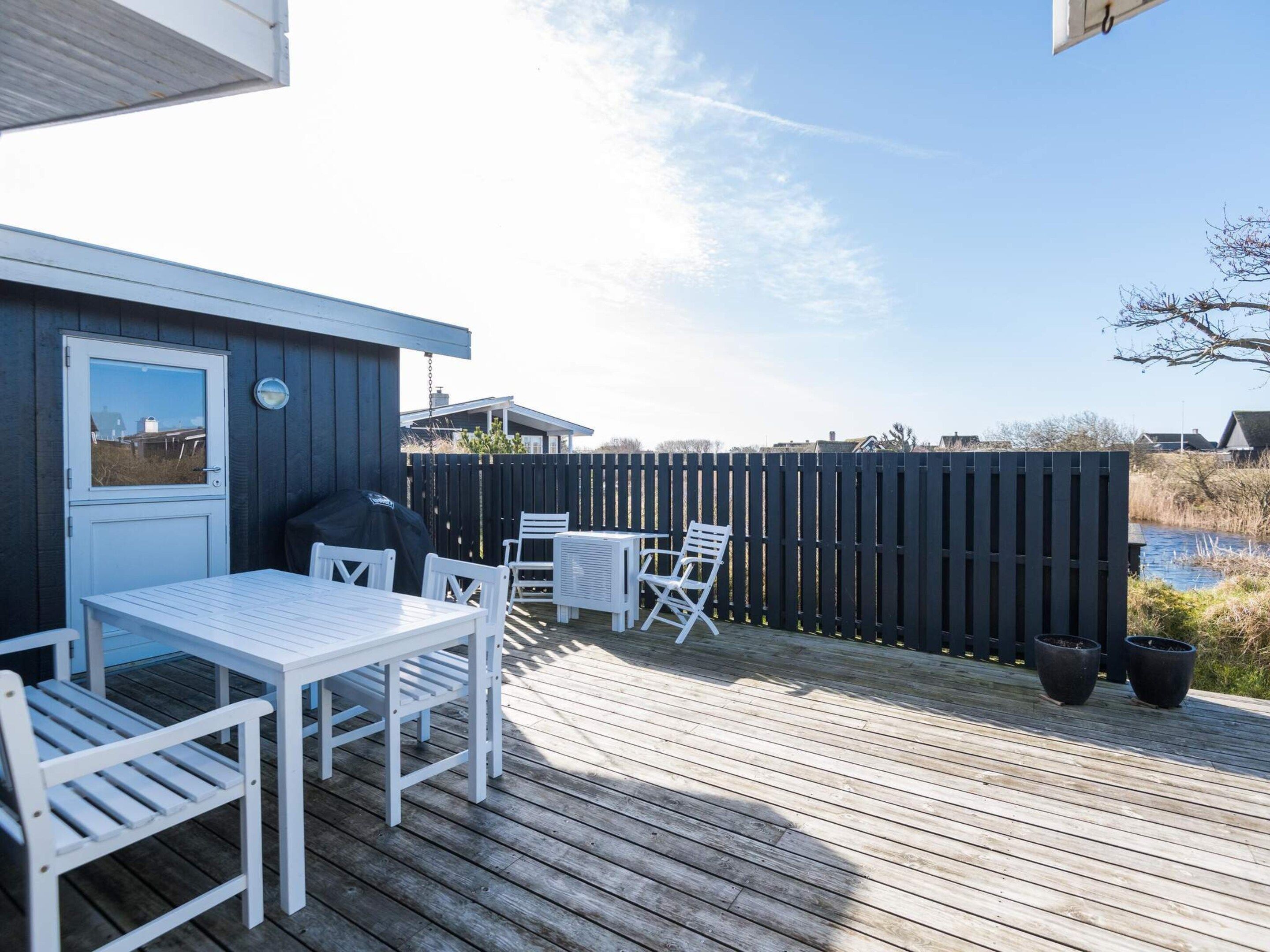 A wooden deck with a table and chairs, a covered grill, and a view of a water body.