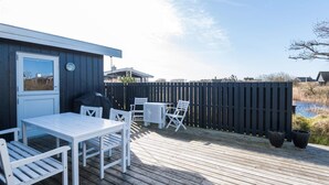 A wooden deck with a table and chairs, a covered grill, and a view of a water body. - 4 Person Holiday Home in Fano (Fano)